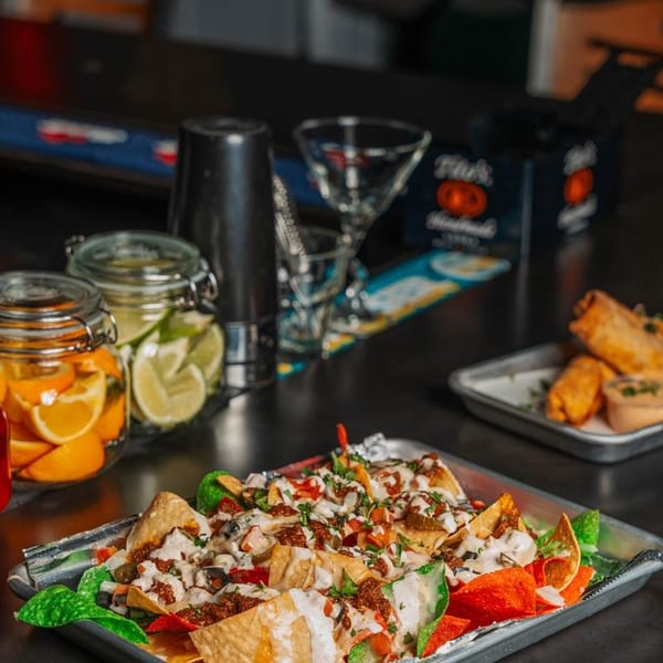 Loaded nachos on a tray with citrus garnishes and barware in the background.