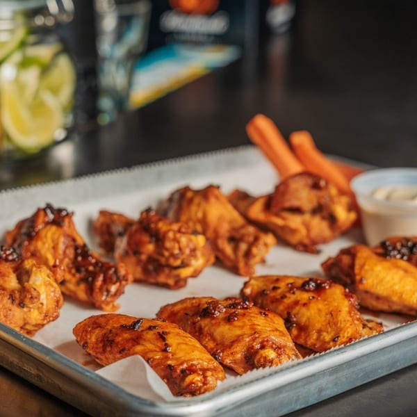A metal tray of glazed chicken wings with carrots, celery, and ranch dressing.
