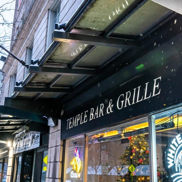 Exterior view of Temple Bar & Grille sign on a snowy day with a Christmas tree visible inside.